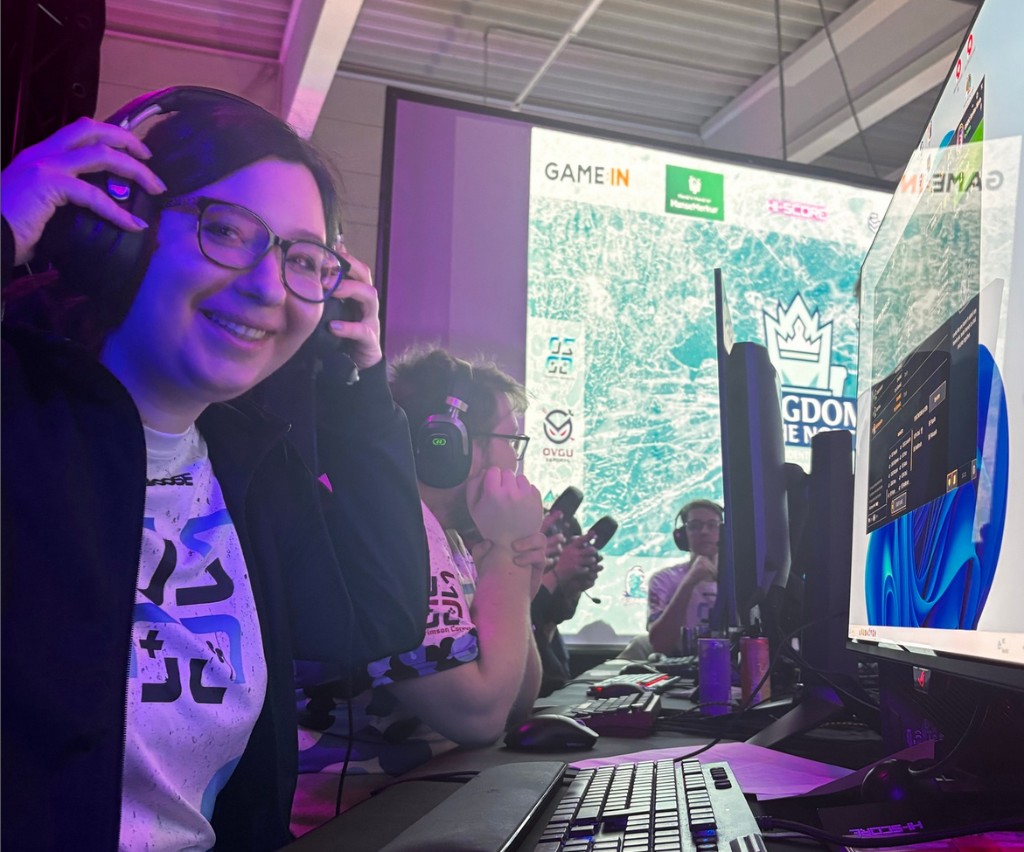 Jana mit Headset an einem Gaming-PC auf einer Bühne, blau-violettes Licht.